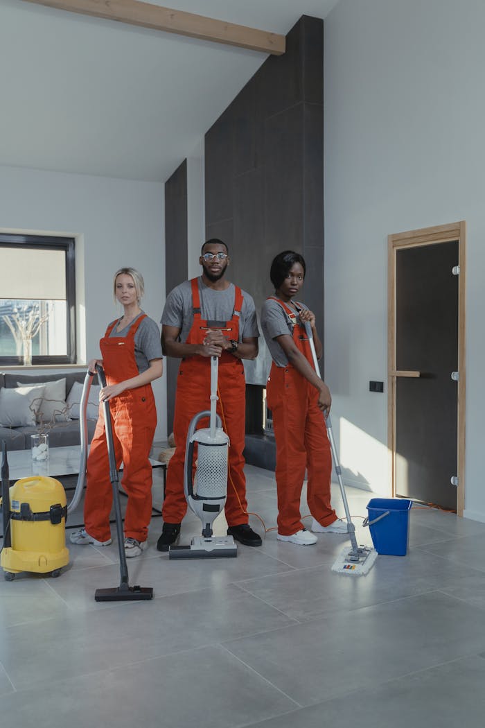 Three professional cleaners in uniform inside a modern home with cleaning equipment.